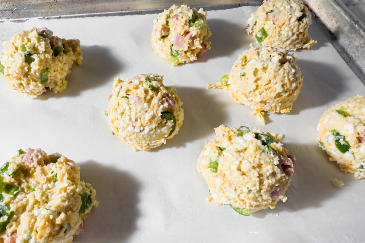 Mounds of uncooked biscuit dough spaced on a parchment-lined baking sheet.