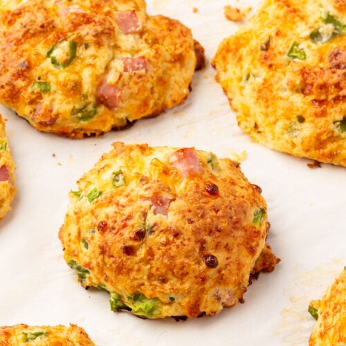 Gluten-free cottage cheese breakfast biscuits baked on parchment paper with browned tops and visible ham and vegetables.
