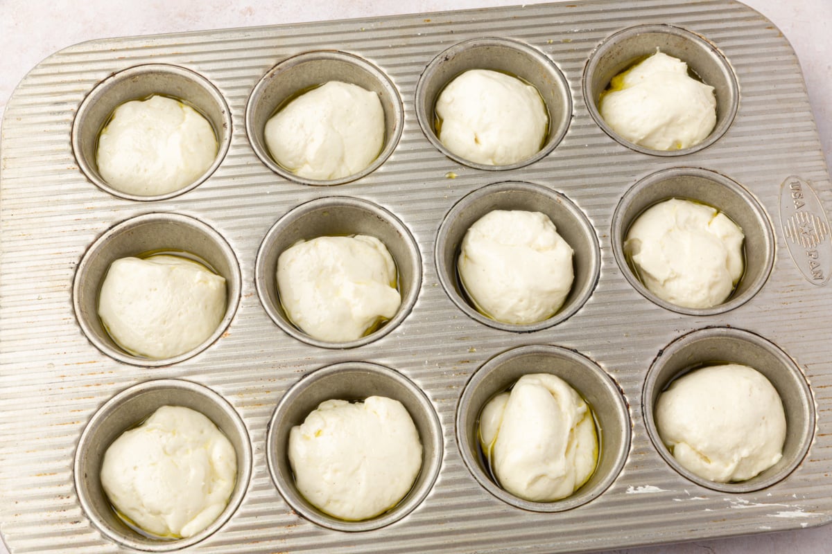 Portioned balls of gluten-free focaccia dough placed in an oiled muffin tin before rising.