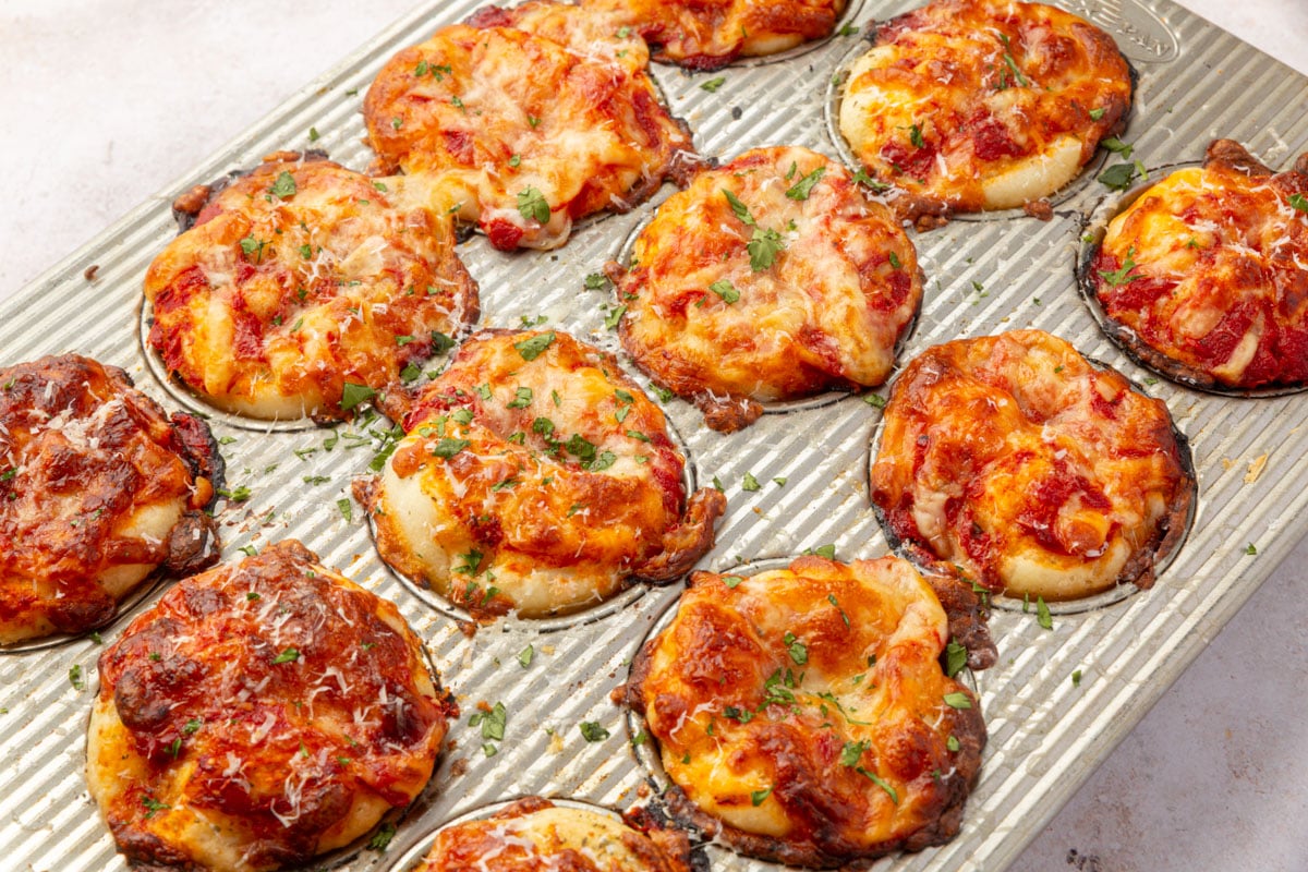 Golden brown gluten-free focaccia pizza muffins just baked in the pan, topped with melted cheese and herbs.