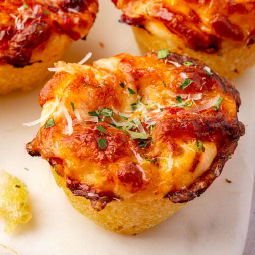 Overhead photo of gluten-free focaccia pizza muffins on a marble board topped with parmesan and herbs.