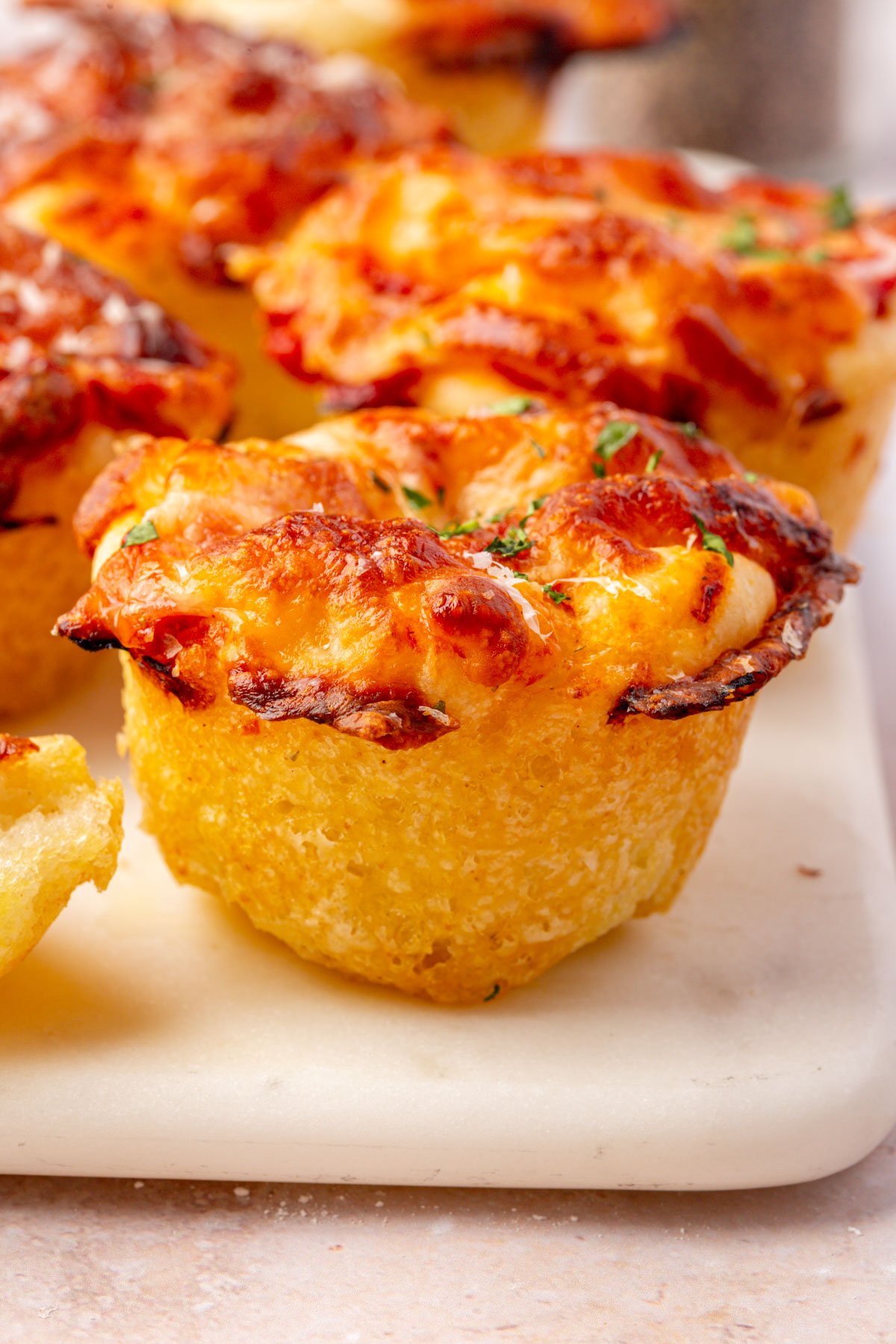 Side angle of gluten-free focaccia pizza muffins showing crisp, golden edges and melted cheese on top.