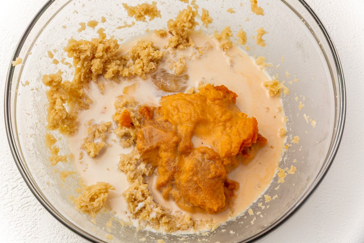 Pumpkin puree and milk added to creamed butter mixture in a glass bowl for gluten-free pumpkin coffee cake.