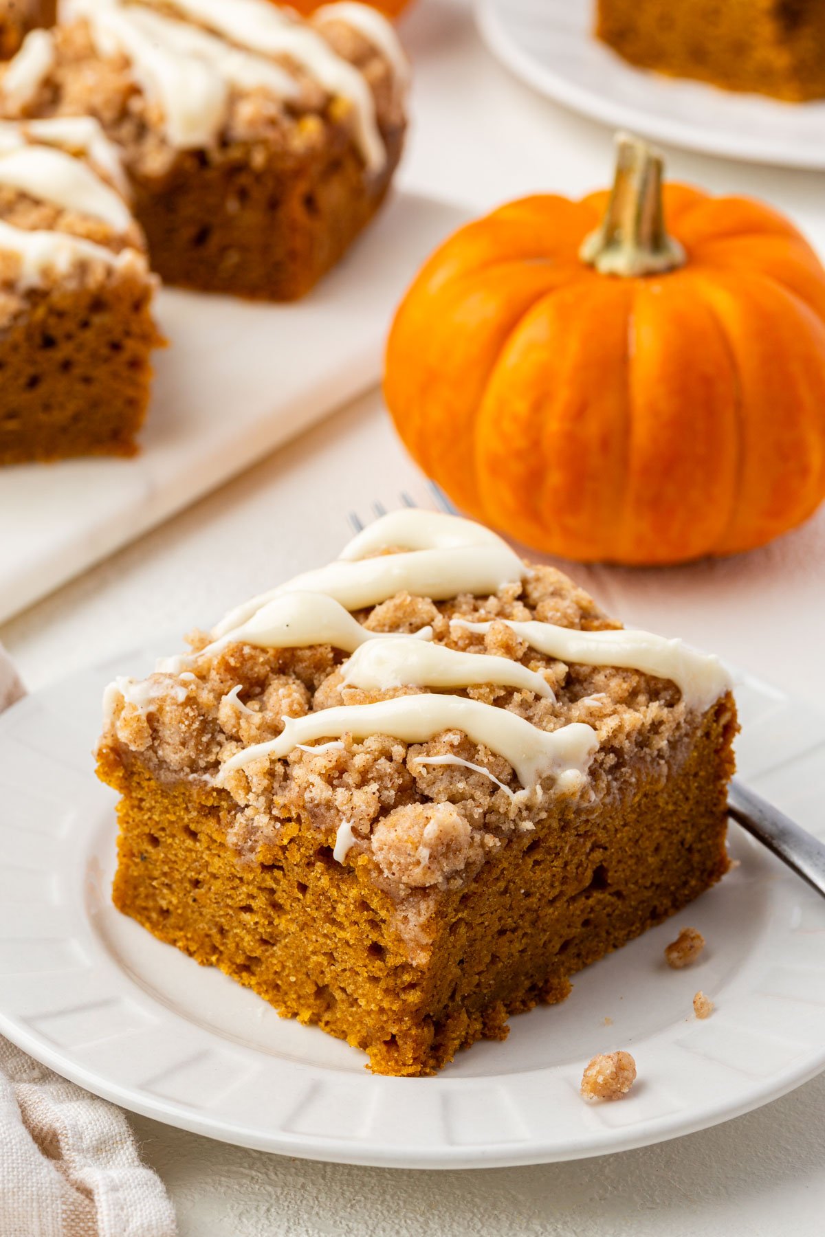 Close-up of a single slice of gluten-free pumpkin coffee cake with streusel topping and cream cheese glaze beside a fork.