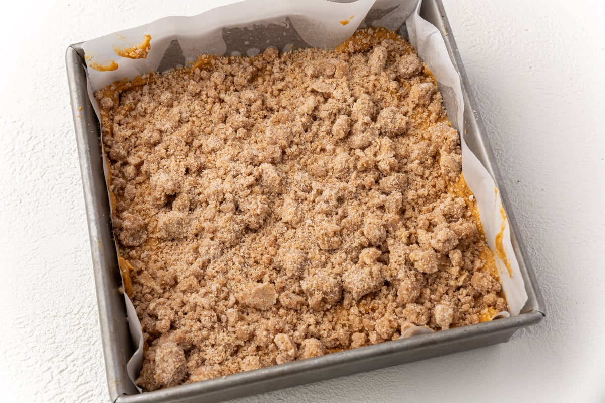 Unbaked gluten-free pumpkin coffee cake in a square pan topped with cinnamon streusel crumb topping.