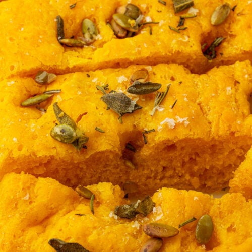 Sliced gluten-free pumpkin focaccia topped with flaky sea salt, rosemary, sage, and pepitas.