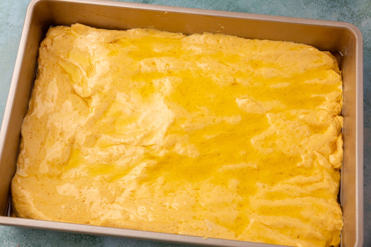 Pumpkin focaccia dough spread in the pan and drizzled with olive oil.