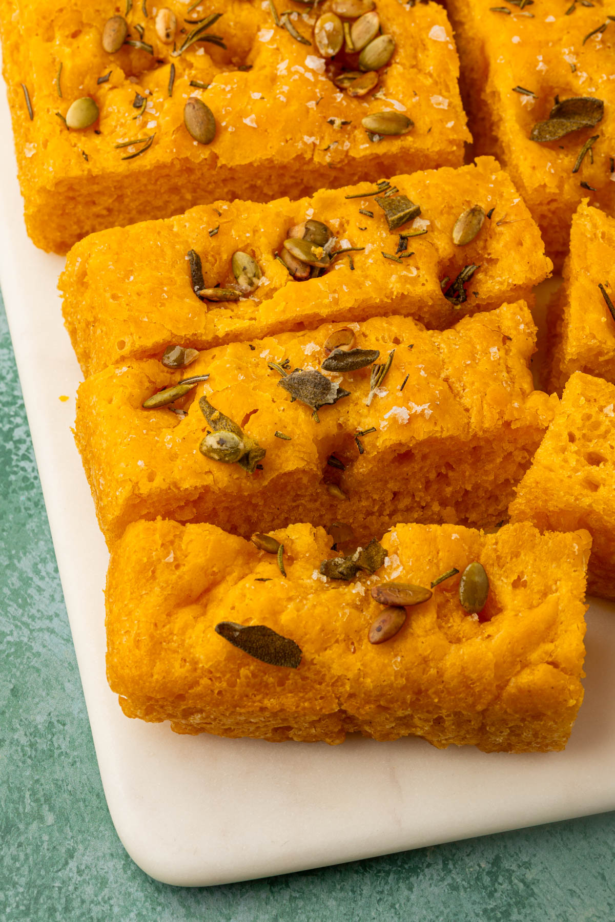 Rectangular slices of gluten-free pumpkin focaccia sprinkled with rosemary, sage, pepitas, and sea salt.