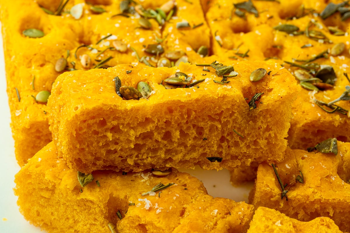 Thick slice of gluten-free pumpkin focaccia highlighting its airy interior and crisp edges.