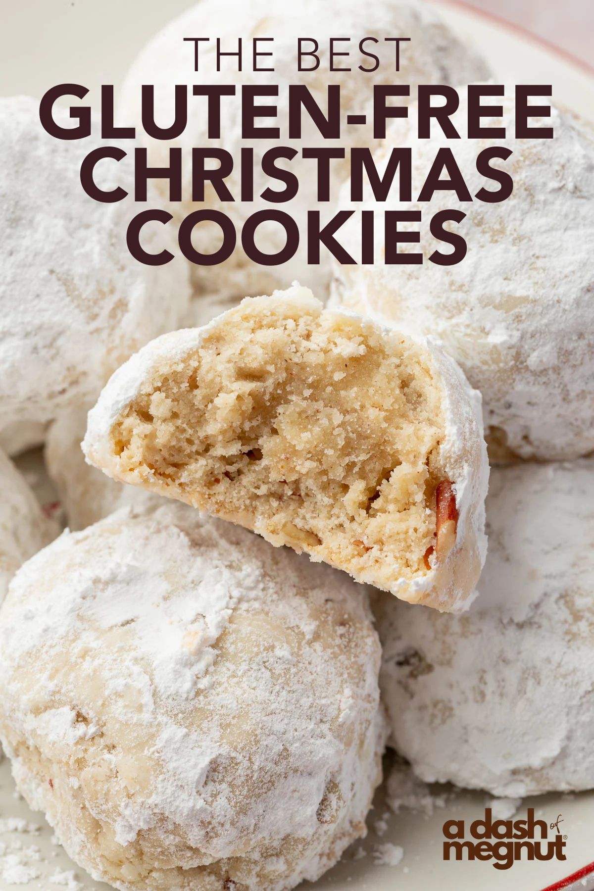 A pile of gluten-free snowball cookies coated in powdered sugar on a white plate with a red rim. One cookie has a bite taken out of it, showing the tender, crumbly inside studded with pecans.