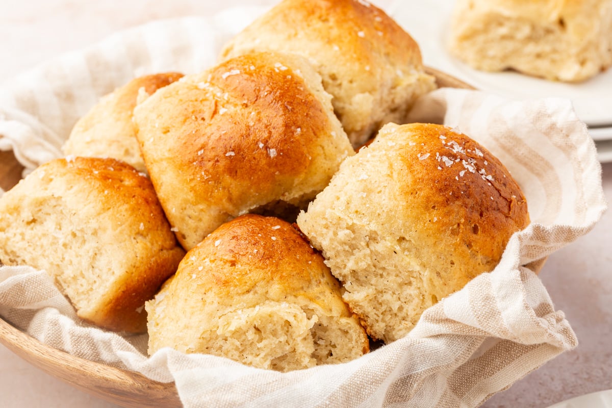Basket lined with a striped towel filled with warm gluten-free dinner rolls.