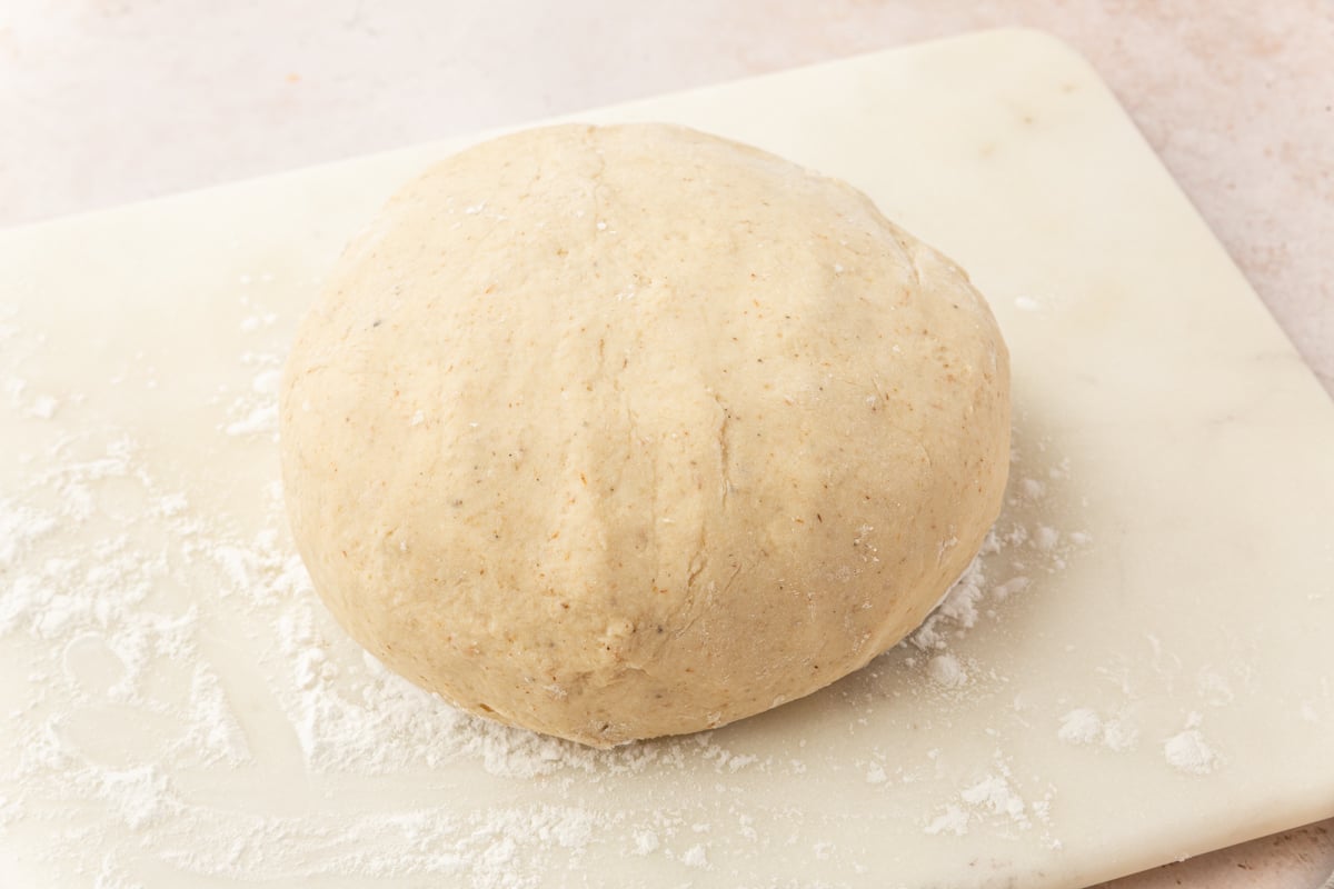 Smooth gluten-free dough ball resting on a lightly floured surface before shaping.