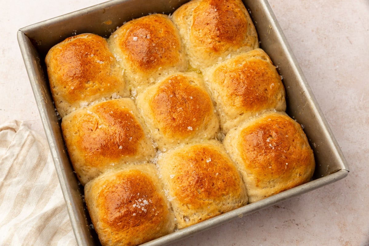 Golden brown gluten-free dinner rolls baked in a square pan, brushed with butter and sprinkled with flaky sea salt.