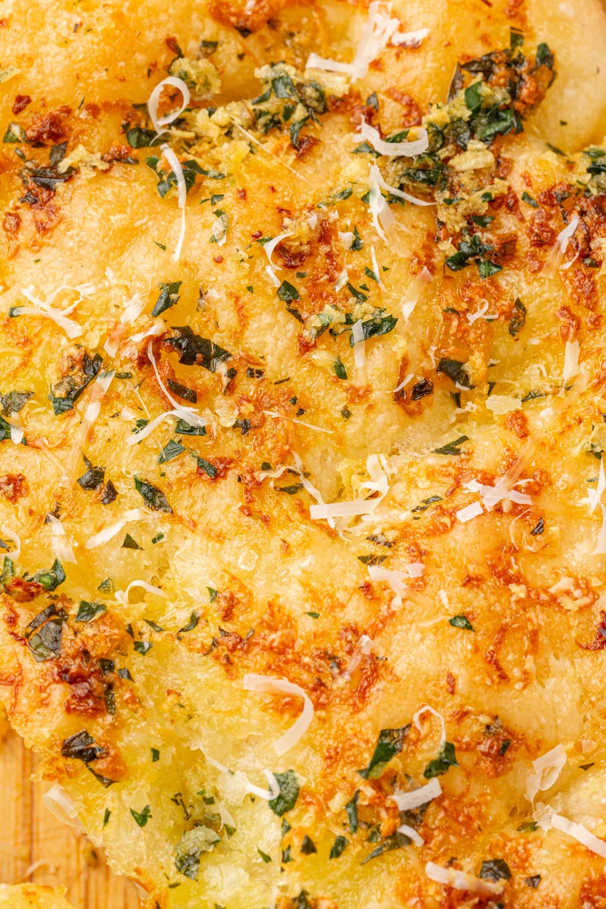 Overhead view of gluten-free garlic butter focaccia with golden dimpled surface topped with parsley, parmesan cheese, and olive oil.