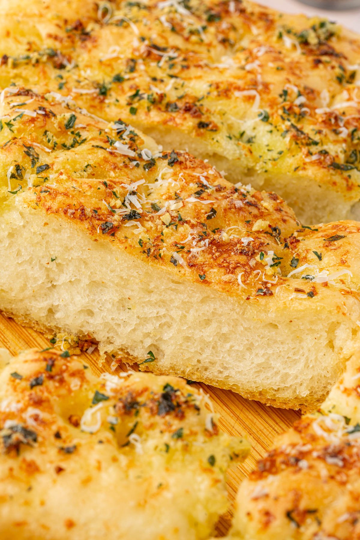 Close-up slice of gluten-free garlic butter focaccia showing light airy crumb texture and golden buttery crust with fresh parsley.