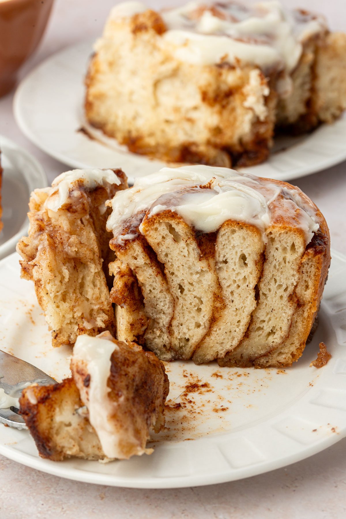 Soft gluten-free cinnamon roll on a plate with a bite cut off to show the fluffy, tender layers inside.