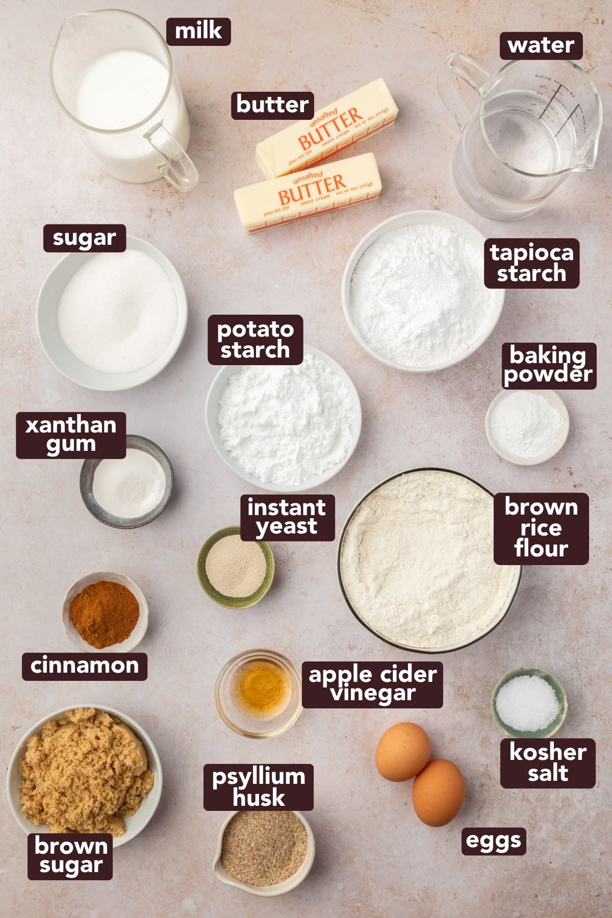Overhead view of labeled ingredients for gluten-free cinnamon rolls, including flour, starches, yeast, sugar, and butter.