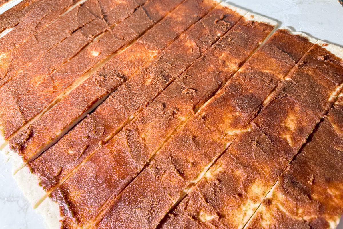 Dough with cinnamon filling cut into even strips before rolling.