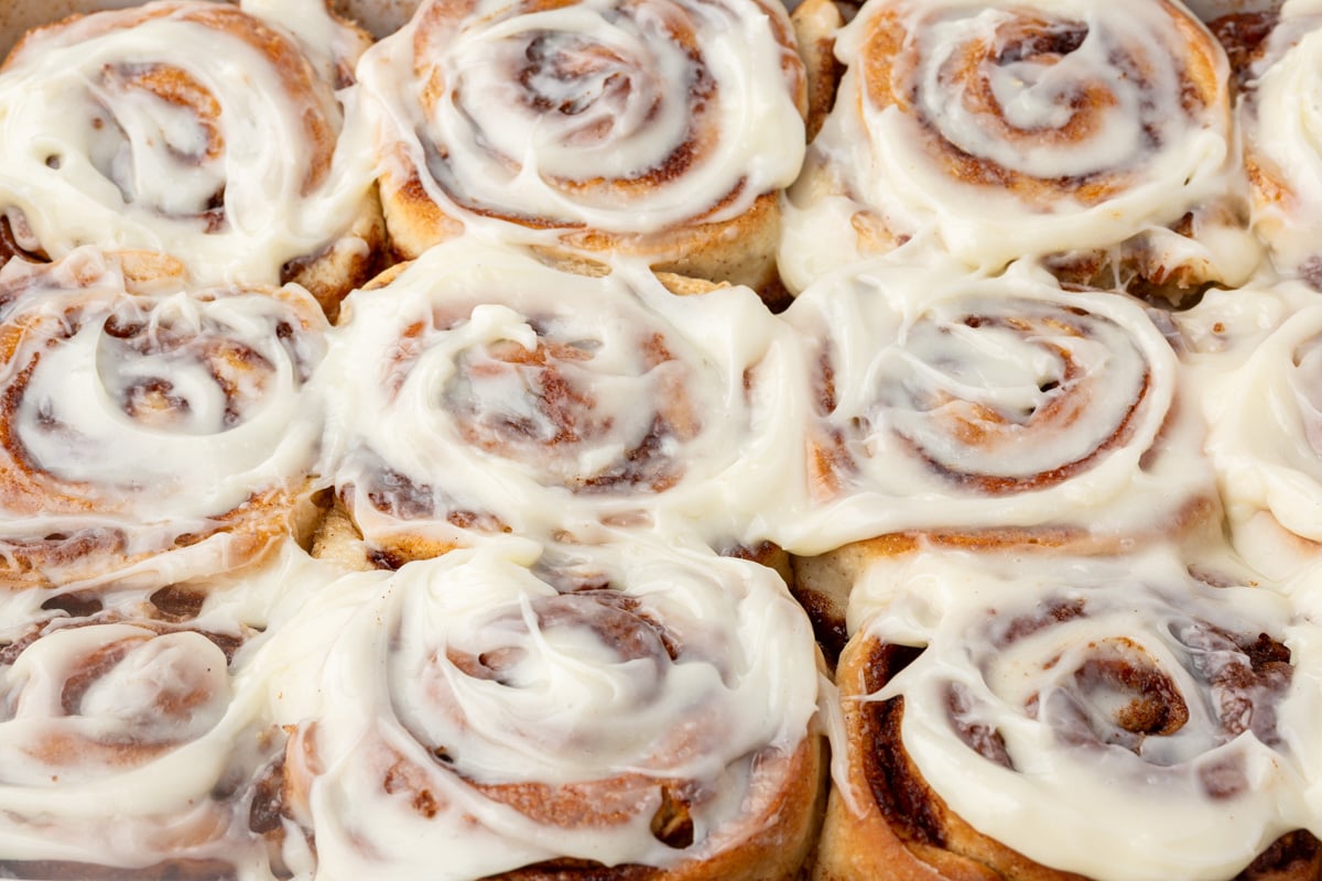 Pan of freshly baked gluten-free cinnamon rolls generously frosted with cream cheese icing.
