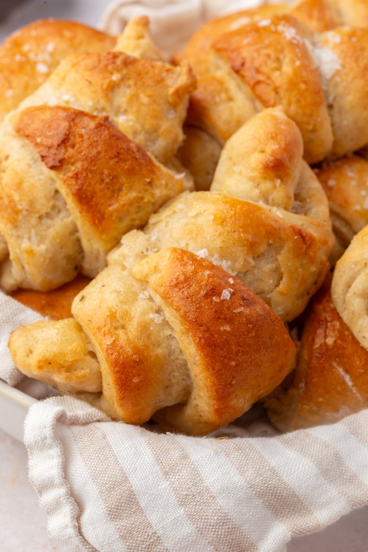 Close up of golden brown gluten-free crescent rolls in a basket with flaky sea salt.