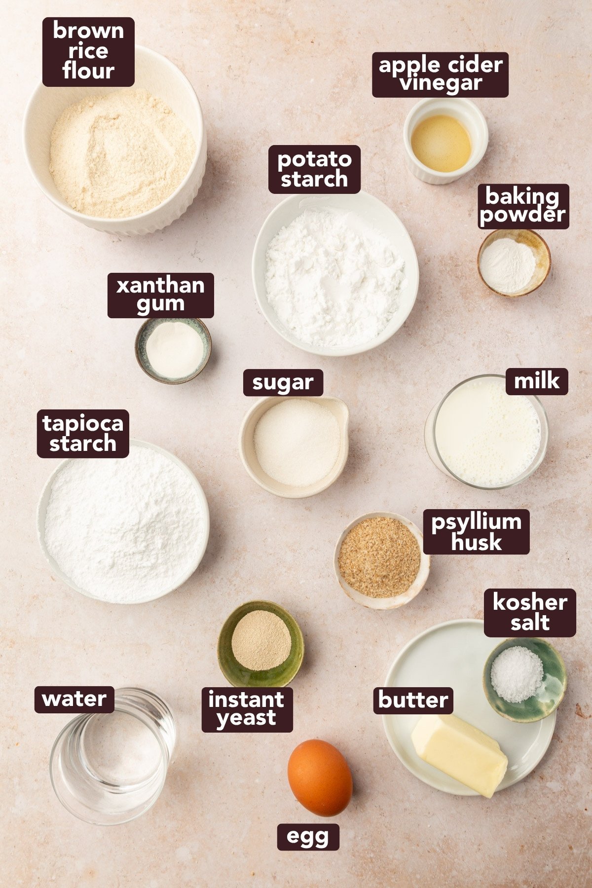 Overhead view of ingredients for gluten-free dinner rolls, including brown rice flour, starches, yeast, psyllium husk, milk, butter, and egg.