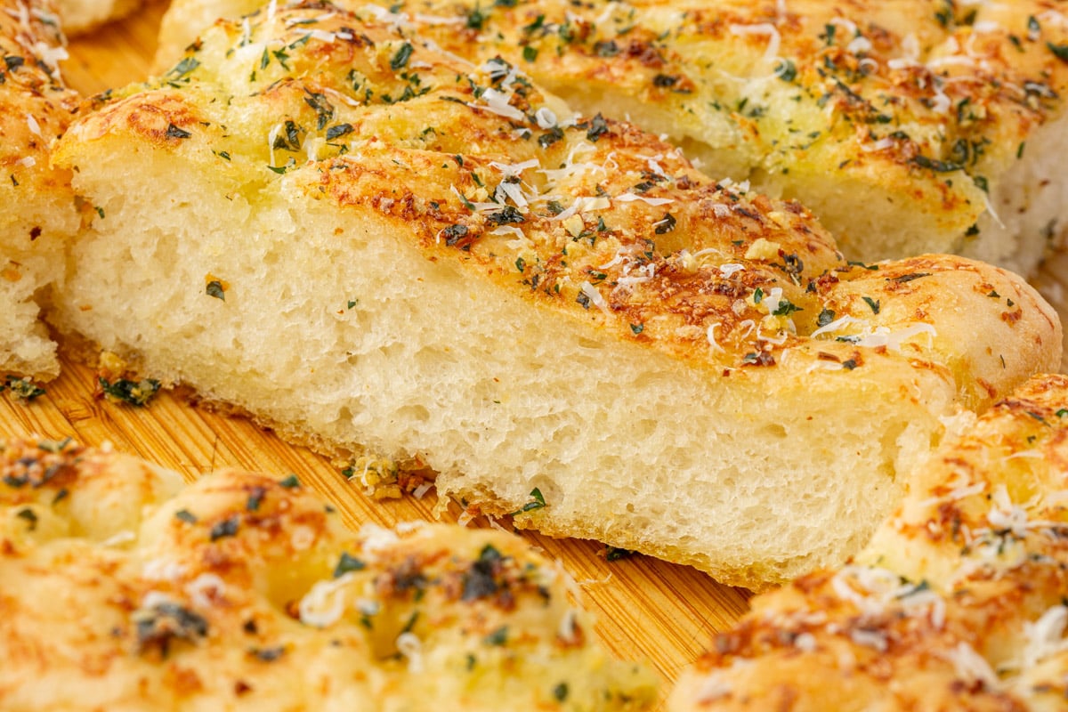 Side view of gluten-free focaccia bread slice revealing open airy crumb structure and crispy garlic butter topping.