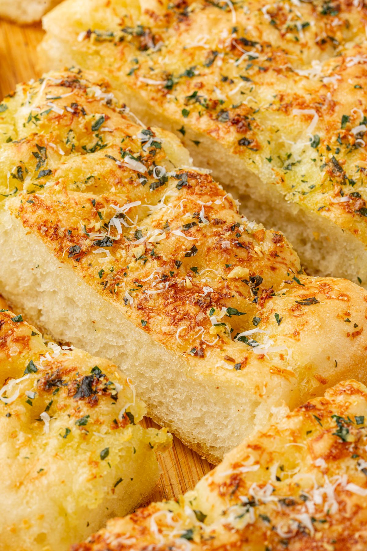 Freshly baked gluten-free garlic butter focaccia slices showing airy texture with golden crust topped with garlic butter, parmesan, and parsley.