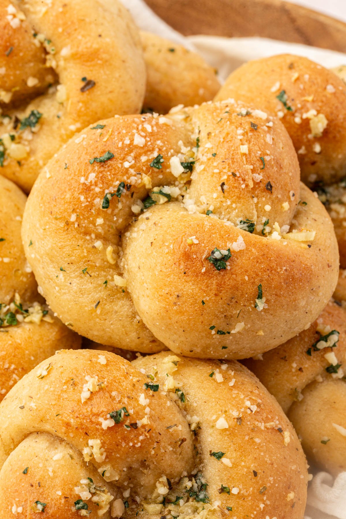Close-up of golden gluten-free garlic knots topped with minced garlic, parsley, and grated cheese.