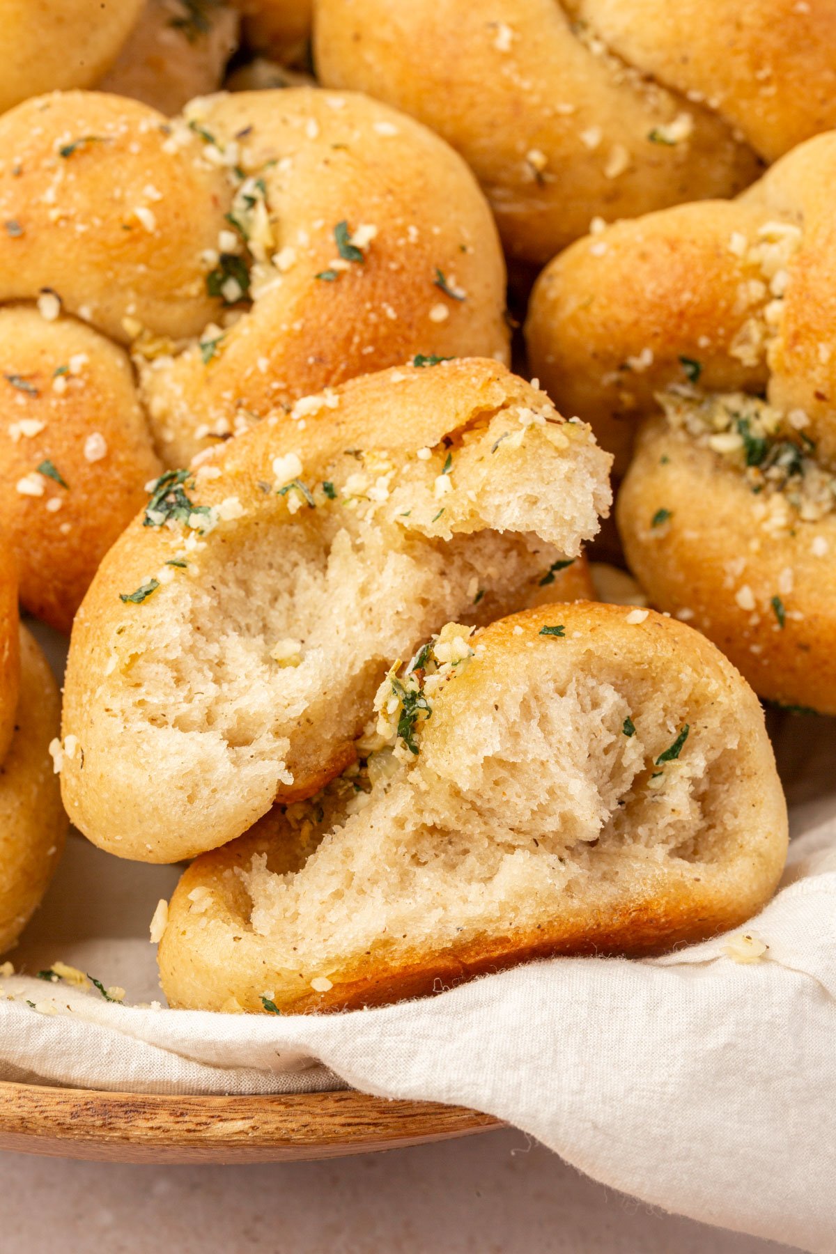 A gluten-free garlic knot split open in a basket, revealing a tender, airy crumb coated in garlic butter and herbs.