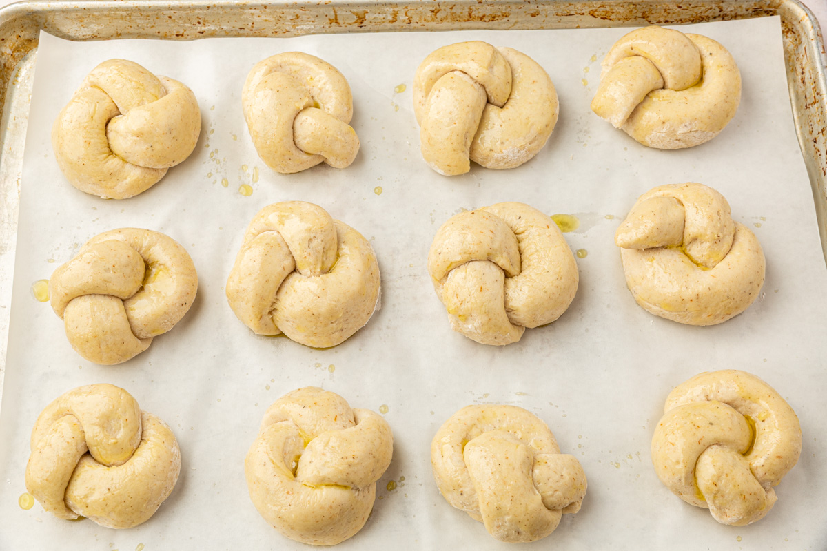 Unbaked gluten-free garlic knots brushed with olive oil on a parchment-lined baking sheet.