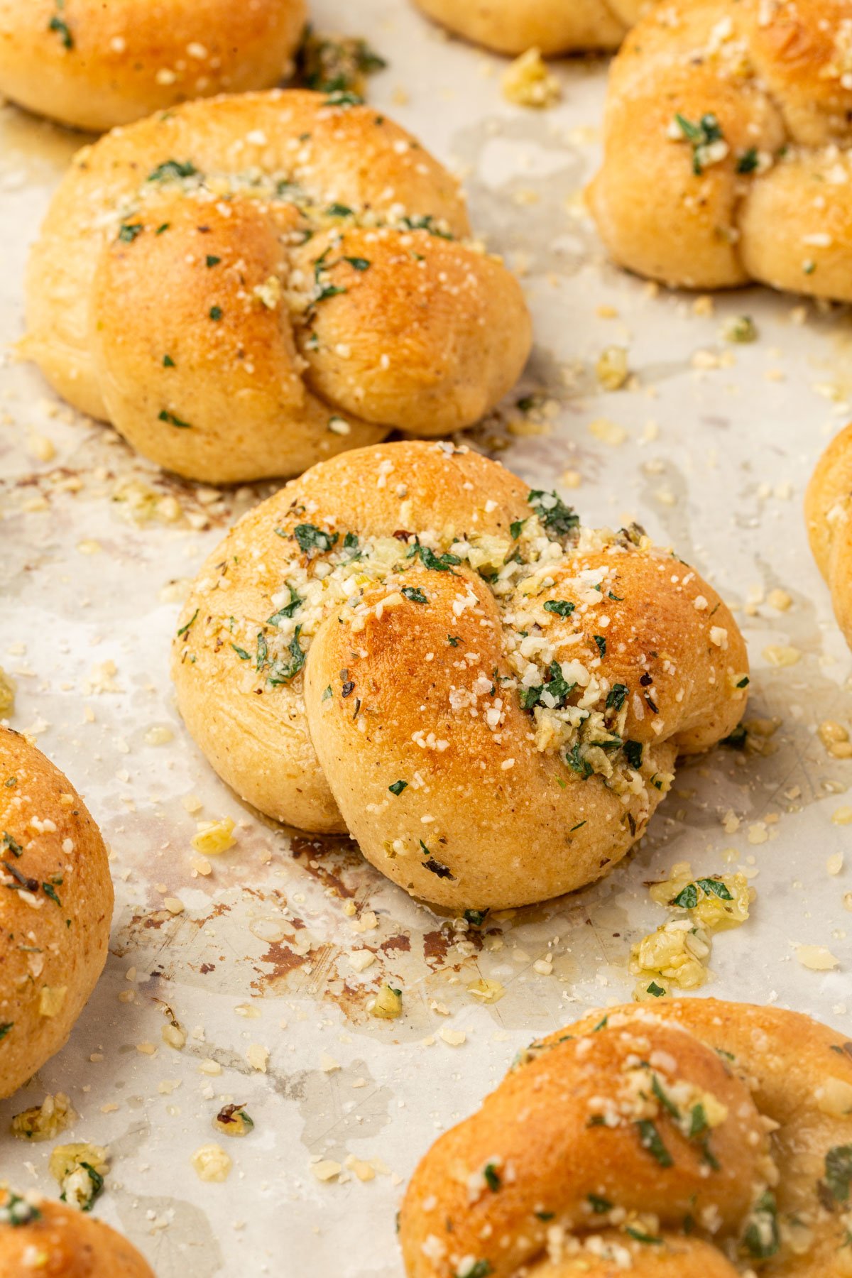 Baked gluten-free garlic knots on parchment paper, coated with garlic butter and sprinkled with cheese and herbs.