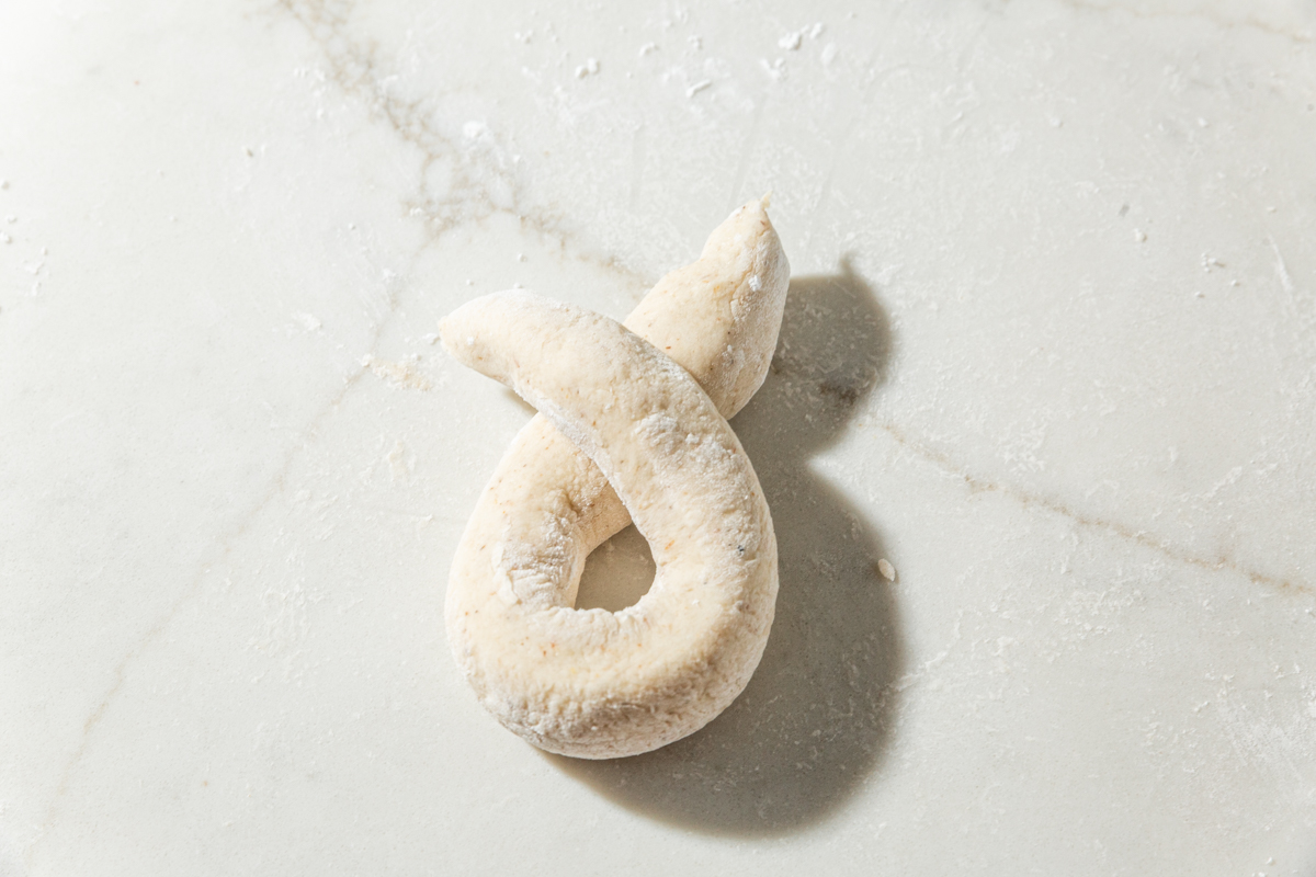 Two ends of a dough rope crossed to show the first step of forming a garlic knot.