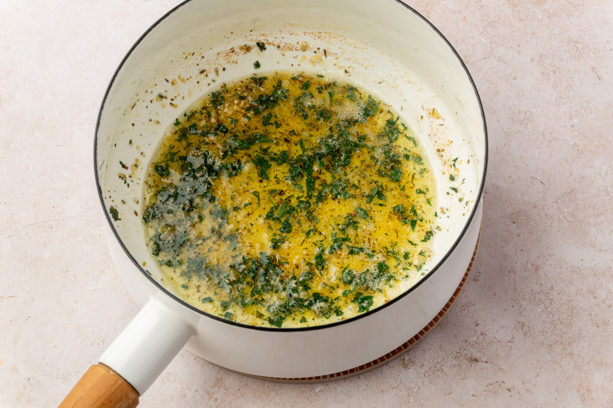 Melted garlic butter with herbs and parsley simmering in a small white saucepan.