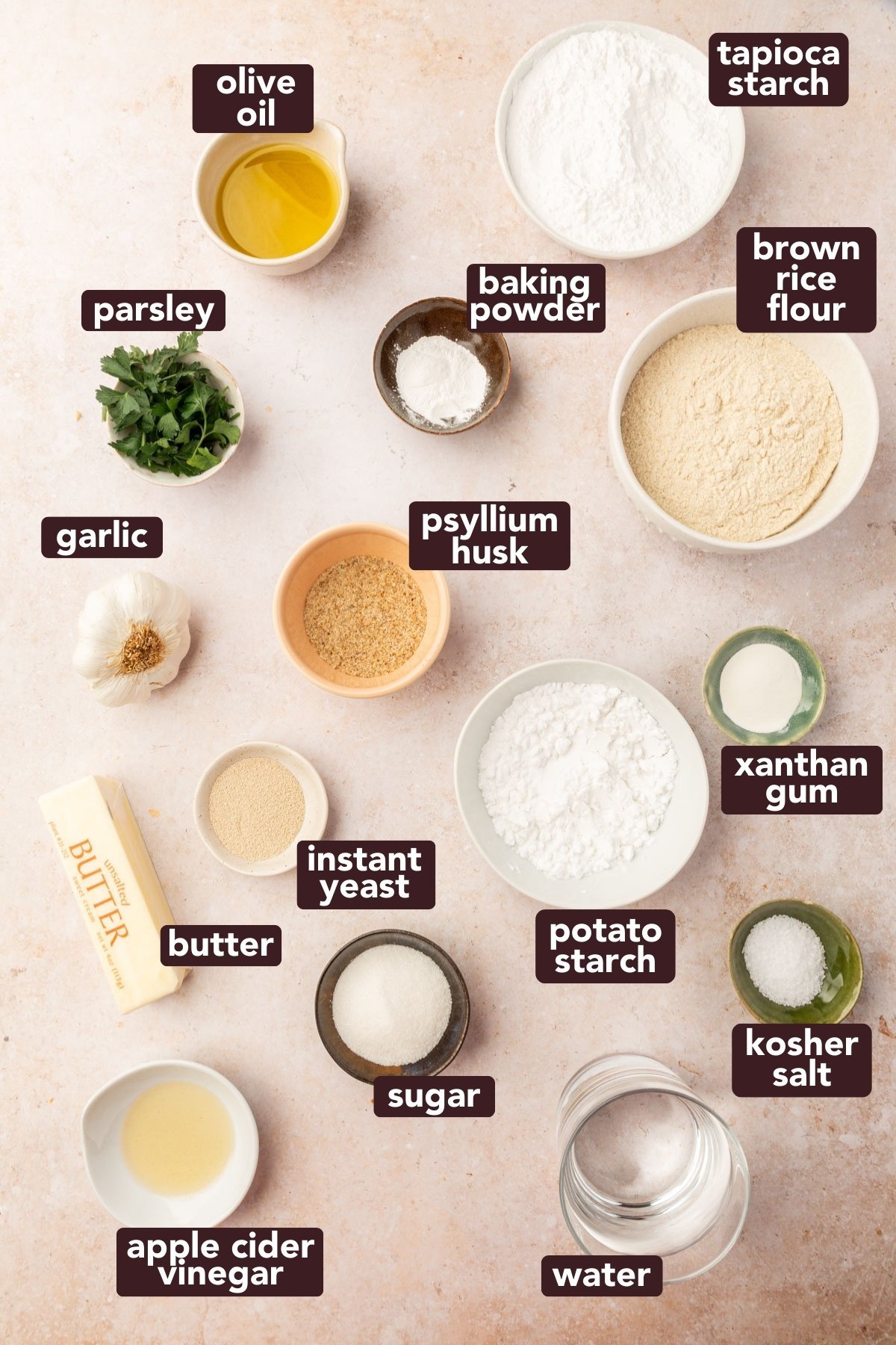 Flatlay of ingredients for gluten-free garlic knots including flour, starches, yeast, psyllium husk, olive oil, garlic, butter, parsley, salt, and water.