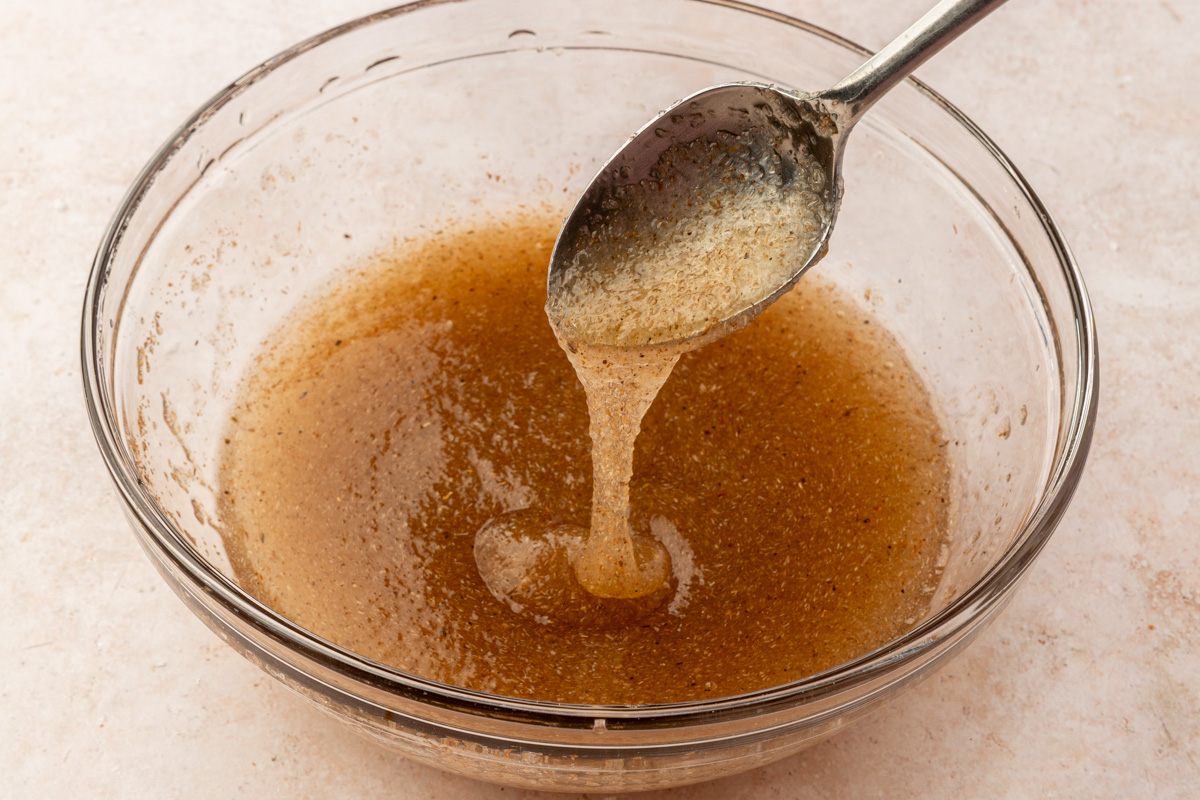 Whole psyllium husk mixed with warm water forming a thick gel being lifted by a spoon in a glass bowl.