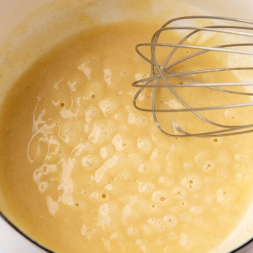 Hand whisking gluten-free roux in a saucepan as it thickens to a smooth, glossy texture.