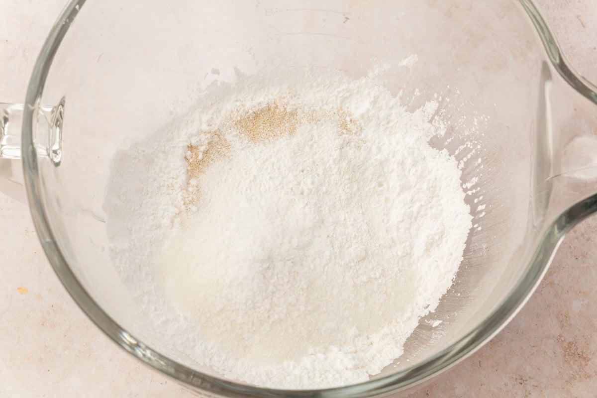 Dry ingredients for gluten-free dinner rolls, including flour, starch, yeast, and salt, in a large glass mixing bowl.