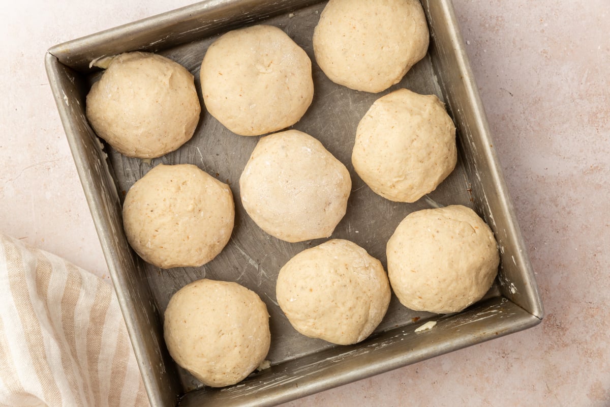 Shaped gluten-free dinner roll dough balls arranged in a metal baking pan before rising.