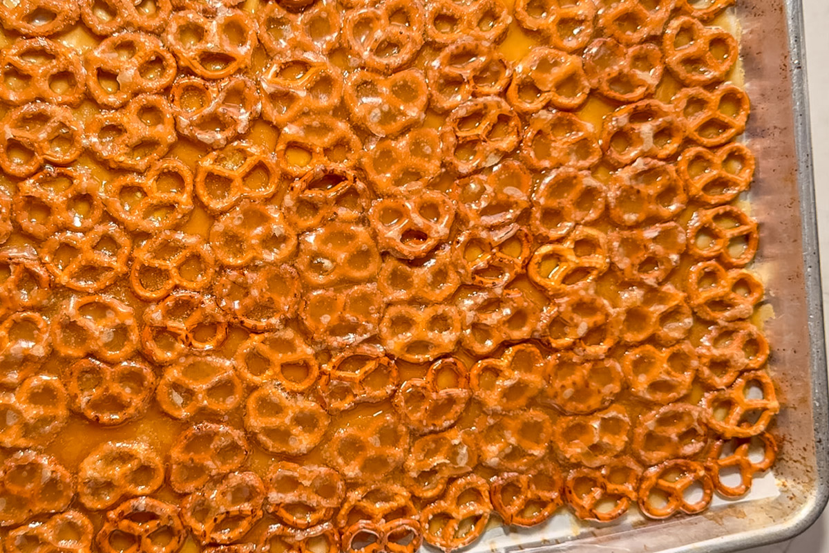 Gluten-free pretzels on baking sheet covered with bubbling golden caramel after 5 minute bake, ready for chocolate chips.
