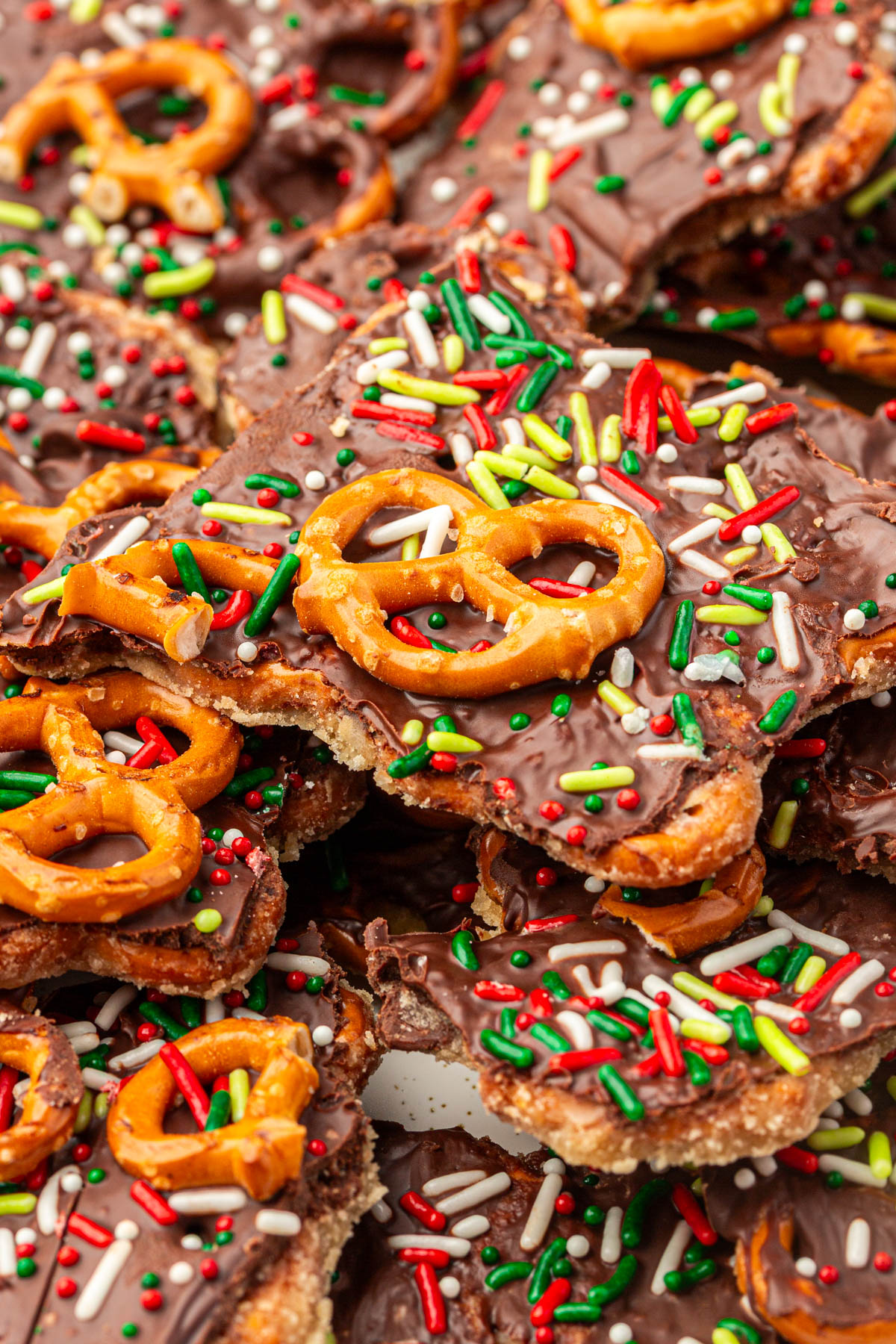 Close-up of chocolate caramel pretzel bark showing layers of pretzels, buttery caramel, melted chocolate, and red, white, and green holiday sprinkles.