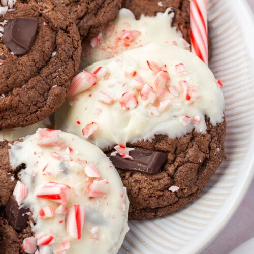 Gluten-free chocolate peppermint cookies on white plate, some dipped in white chocolate with crushed candy canes, others plain with chocolate chunks.