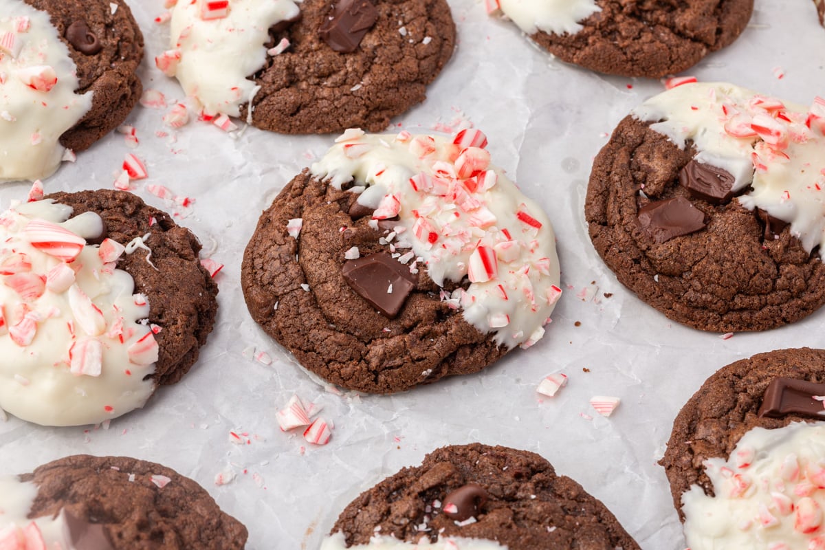 Gluten-free chocolate peppermint cookies cooling on parchment paper, some dipped in white chocolate with crushed candy canes.