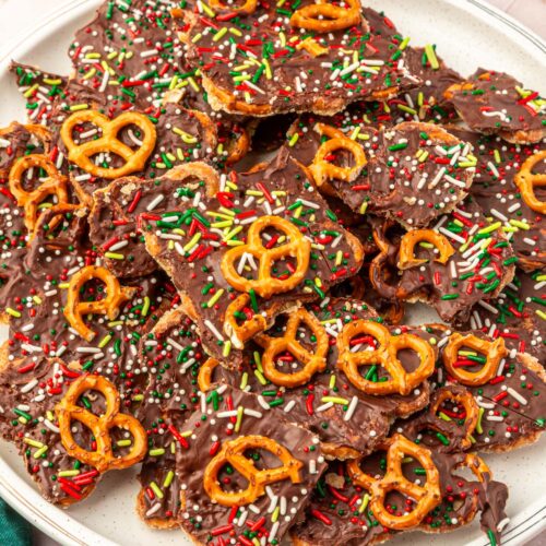 White serving platter filled with pieces of Christmas pretzel bark topped with colorful sprinkles, chocolate chips, and crushed gluten-free pretzels.