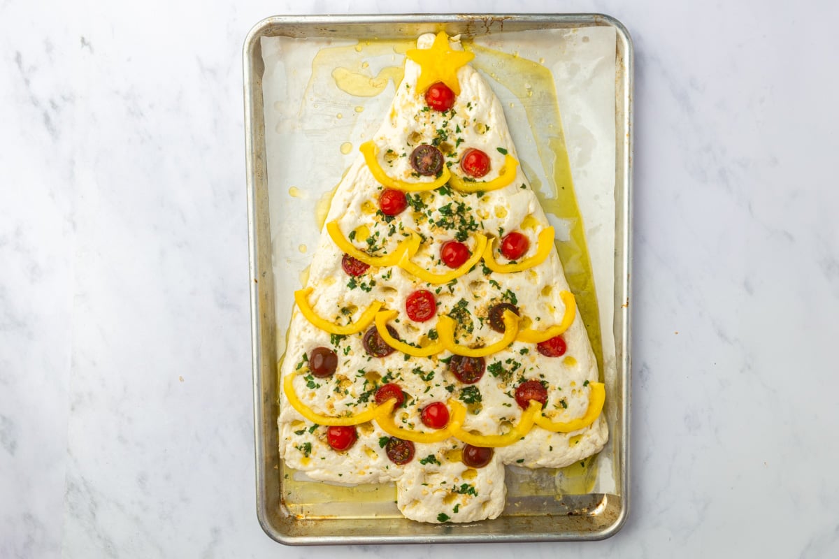 Christmas tree focaccia decorated with yellow pepper star and garland and cherry tomato ornaments before baking.