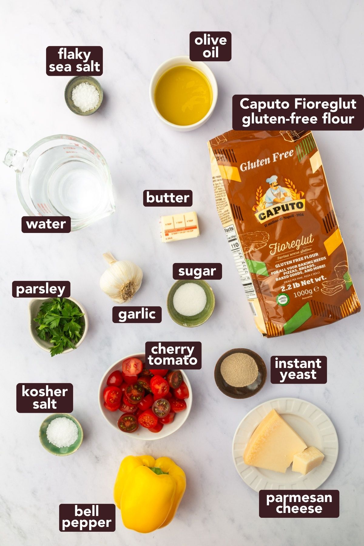 Labeled ingredients for gluten-free Christmas tree focaccia including Caputo Fioreglut flour, cherry tomatoes, yellow bell pepper, parmesan, butter, olive oil, garlic, parsley, yeast, sugar, salt, and water.