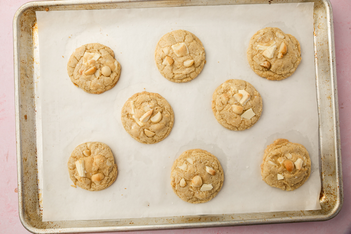 Baked gluten-free white chocolate macadamia nut cookies cooling on a parchment-lined sheet pan.