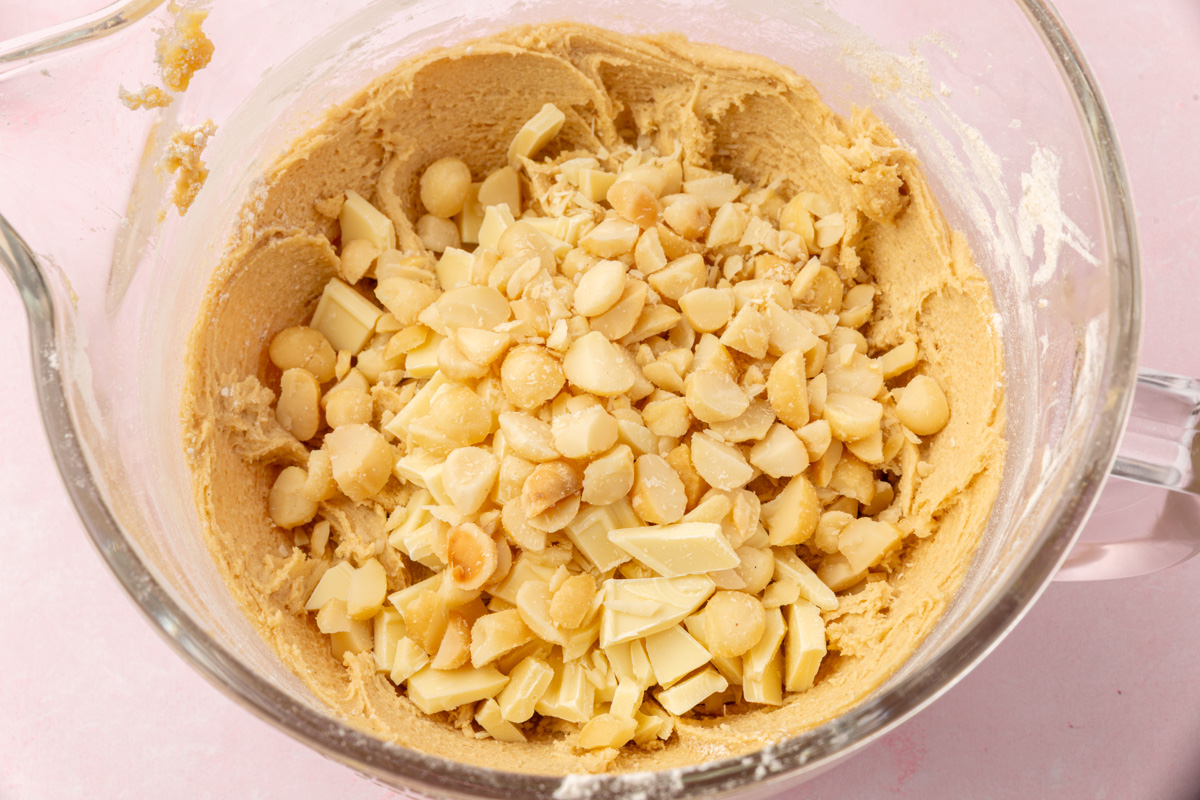 Chopped white chocolate and macadamia nuts added to cookie dough in a mixing bowl.