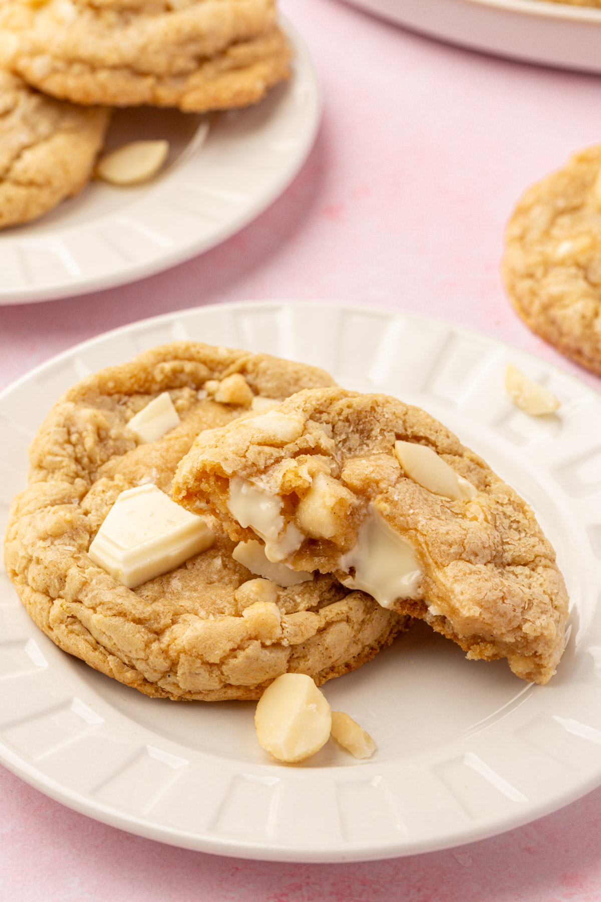 A gluten-free white chocolate macadamia nut cookie broken open on a plate with melted white chocolate inside.