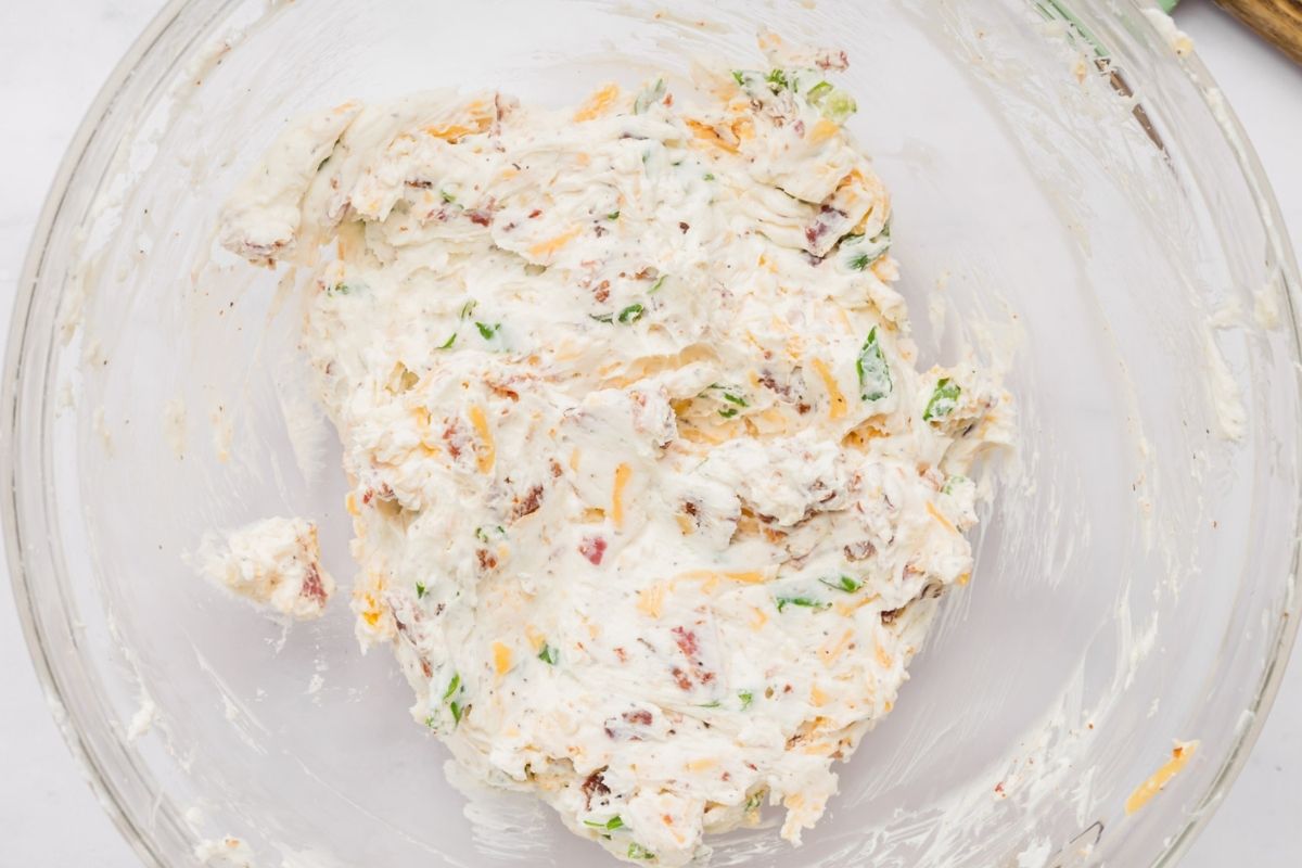 Cream cheese filling mixed with cheddar, bacon, and green onions in a glass bowl.