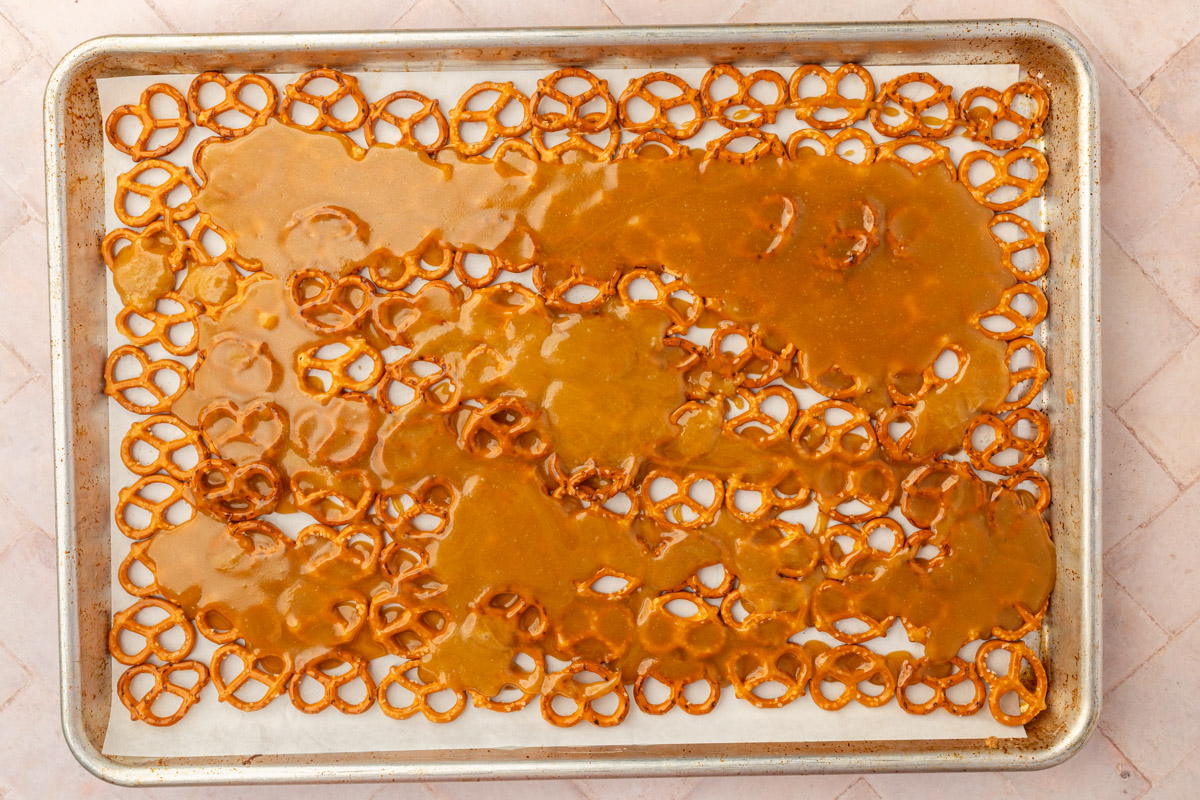 Hot caramel sauce poured over gluten-free pretzels on baking sheet before baking.